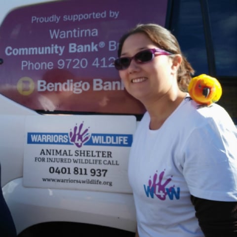 Warriors 4 Wildlife group representative in front of bus branded Wantirna Community Bank Branch of Bendigo Bank and Warriors 4 Wildlife. The group representative has a yellow bird on her shoulder.