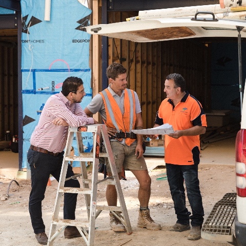 Three men standing on a construction site looking at plans on paper.