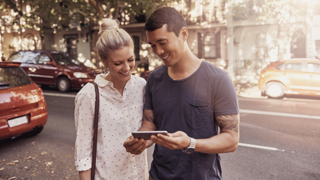 Millennial couple on a metropolitan street discussing property listings displayed on his mobile.
