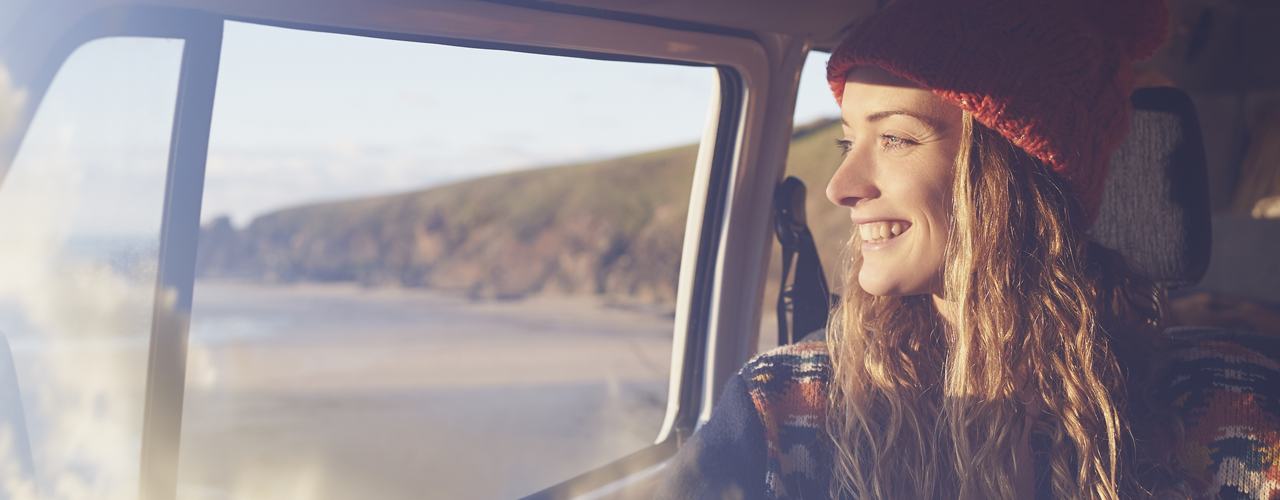 A girl wearing a beanie, smiling and looking out the car window 