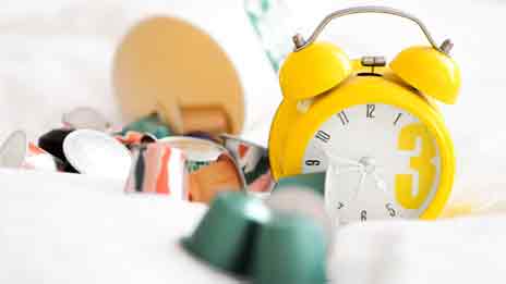 A yellow alarm clock nestled amongst an assortment of coffee machine pods.