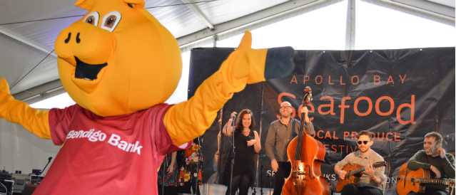 Apollo Bay Community Bank Branch mascot, a big yellow pig, dancing at a community music event sponsored by the branch.