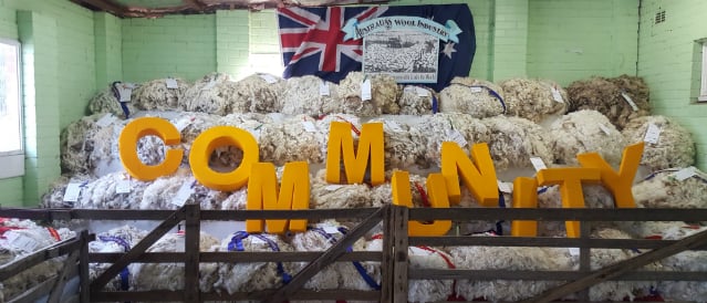 Big yellow letters spelling out the word 'community' sitting in a pen of wool.