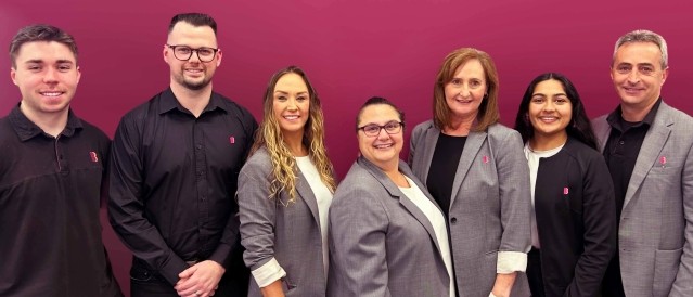 Group of staff standing in front of a plum-coloured background