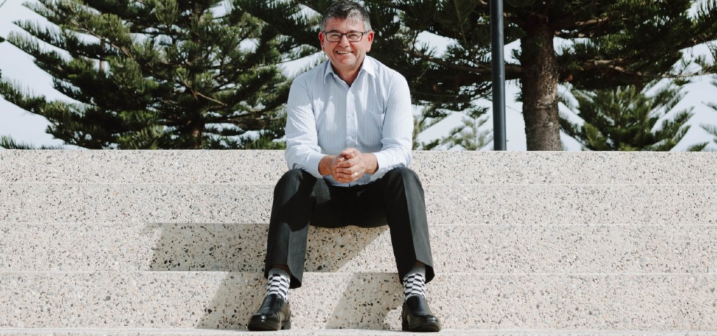Image of David, Branch Manager of Busselton and Dunsborough Community Bank branches of Bendigo Bank, sitting outdoors on large steps with trees in the background.