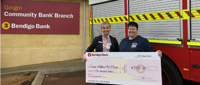 Two people next to an emergency services vehicle holding a large novelty cheque representing a grant from Gingin Community Bank Branch.