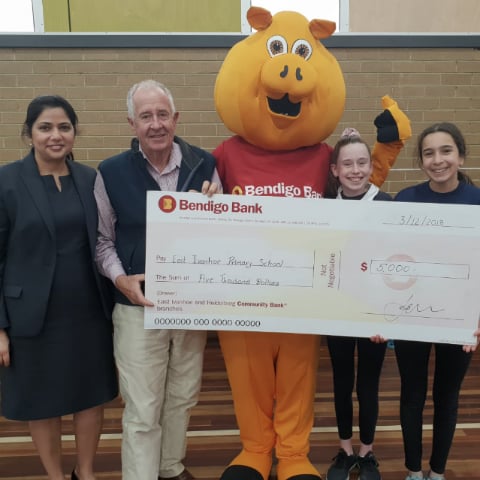 Branch staff and board members pictured with Piggy and two local students holding a novelty cheque.