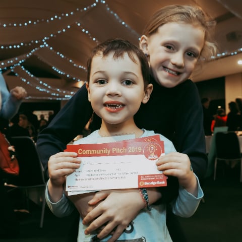Two children who attended the Heidelberg Community Pitch night holding $100 community pitch dollars.