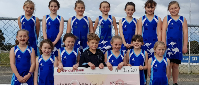 Young netballers with a large novelty cheque representing a grant for their club from Heyfield Community Bank Branch.