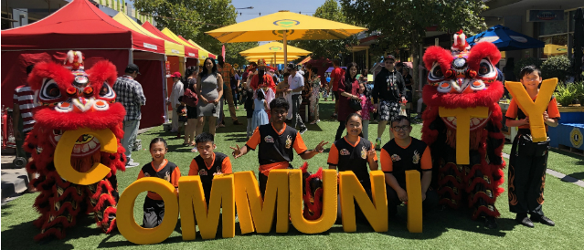 Chinese dragons and people holding large yellow letters spelling the word 'community' at an event funded by Altona and Laverton Community Bank branches.