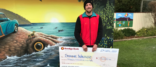 Artist funded by Sheffield Ralton Community Bank Branch standing in front of his mural with a large novelty cheque.