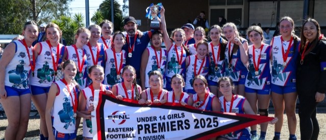 A group of young female football players hold a trophy and premiership flag.