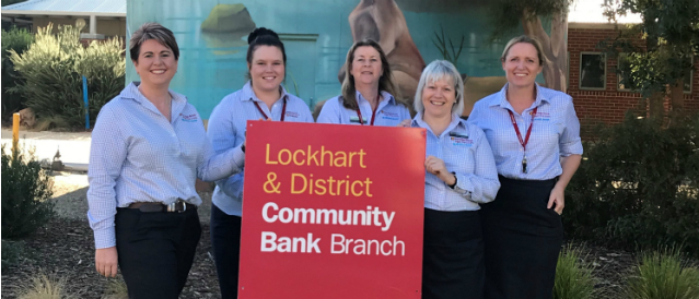 Lockhart Community Bank Branch staff standing outside the branch holding a  Community Bank sign.