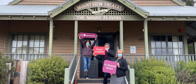 Branch manager and two local grant recipients holding signs out the front of Mountview Theatre that say we love community, grant recipient and a shared return. 