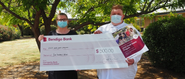 Two branch staff members holding a large bank cheque and poster to promote the 2020 Small Grants Program.