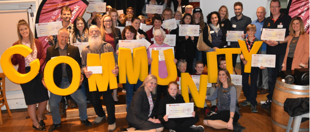 A group of people holding big yellow letters spelling the word 'community' and cheques celebrating a grants program run by Monbulk Community Bank Branch.