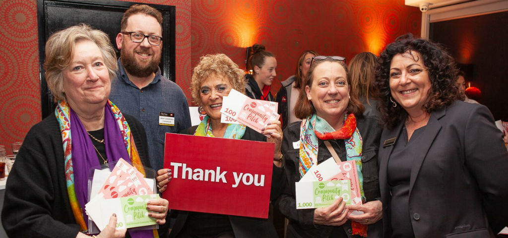 Community members and Mt Eliza branch staff holding thank you sign and community pitch money celebrating the investment back to community groups through the Mt Eliza Community Pitch Program.
