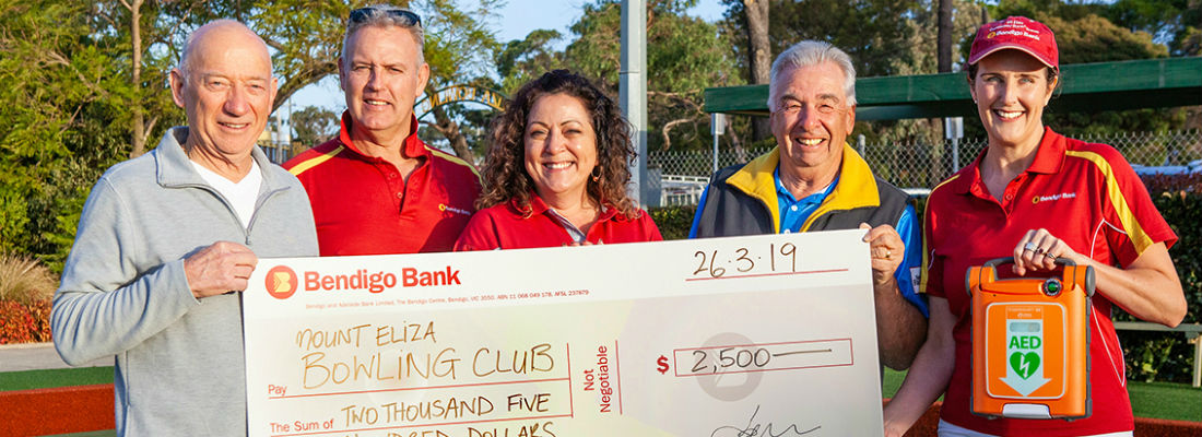 Mount Eliza Community Bank Branch staff and community representatives holding a large novelty cheque and a defib unit to signify a Community Bank branch grant.