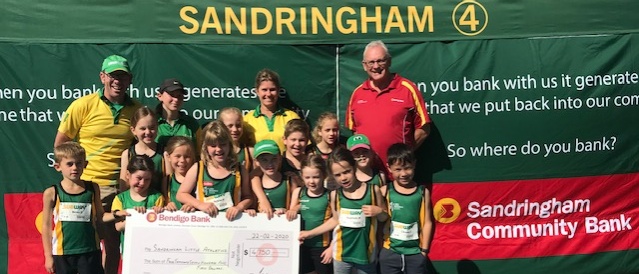 Community sporting group at athletics track with athletes holding 'Helping our community grow' banner.