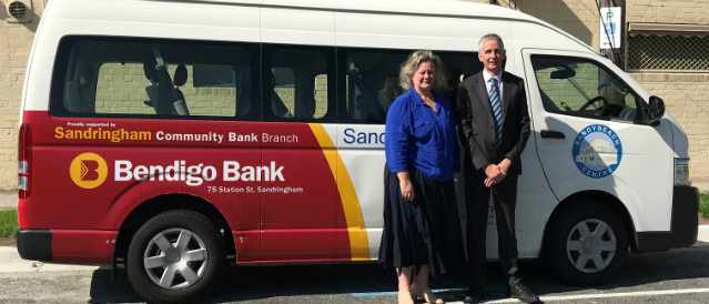 Two people standing next to a bus sponsored by Sandringham Community Bank Branch.