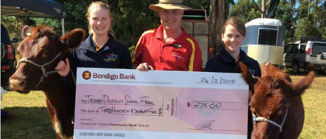 Two children and a Nubeena Tasman Community Bank Branch director with two cows and a novelty cheque to represent a funding contribution to the local cattle event.