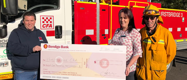 A Community Bank staff member presents a big cheque to the Hustbridge CFA in front of a fire engine