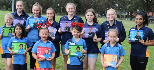 Group of girl guides holding guide handbooks ranging from level one to level five.