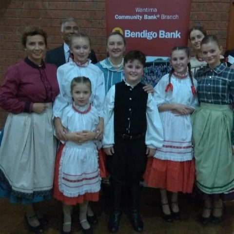 Group of adults and children dressed to celebrate a Hungarian Gala standing in front of a Wantirna Community Bank Branch banner.