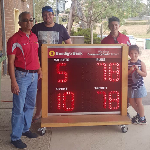 Two branch staff members from Wantirna standing with a male adult and female child with a scoreboard sign for cricket.
