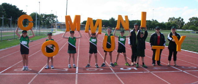 Athletes on a running track hold up big yellow letters spelling out the word 'community' in recognition of a grant for the athletics club from Wantirna Community Bank Branch.
