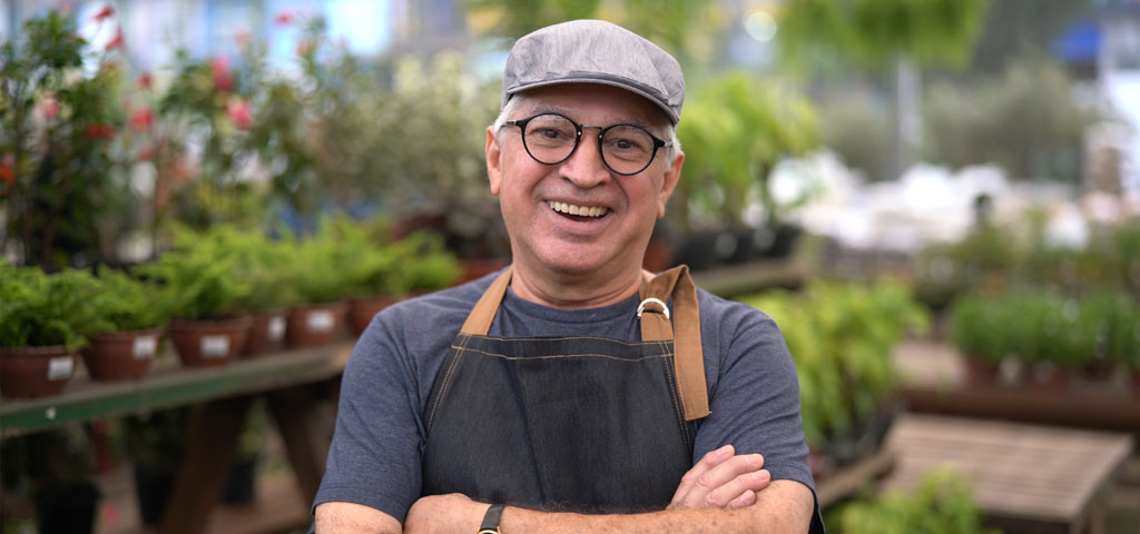 Owner of a garden nursery smiling in front of his plants.