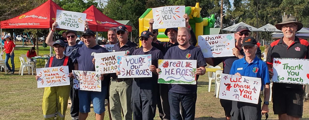 Members of fire brigade holding signs acknowledging the residents of Wooroloo as the real heroes.