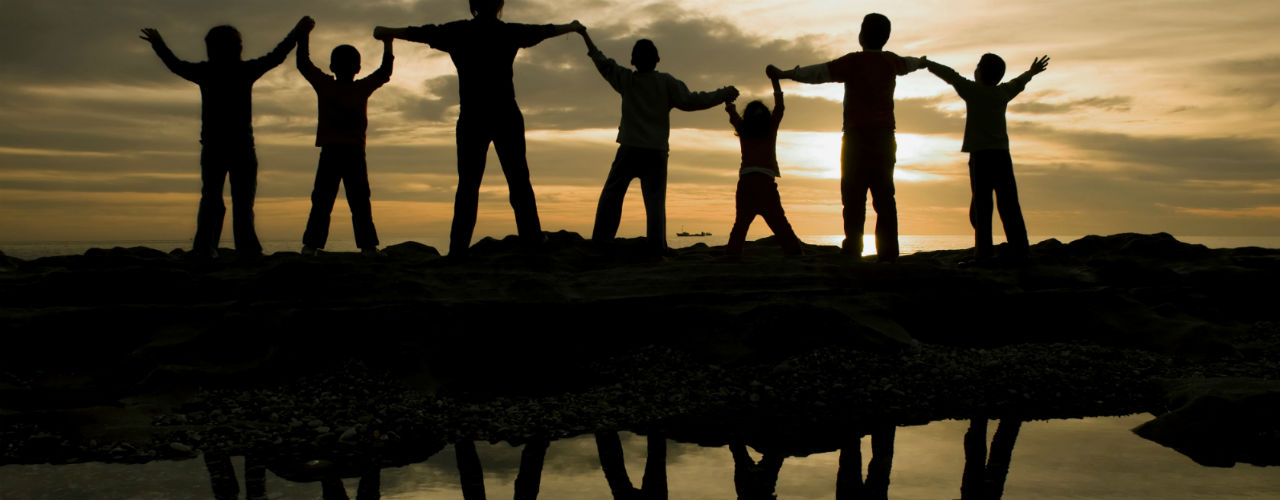 Image of seven people in darkness holding hands with reflection of them in water.