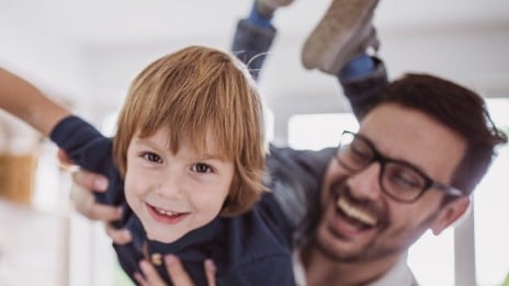 Father laughing as he lifts son up on one shoulder while the son pretends to be flying