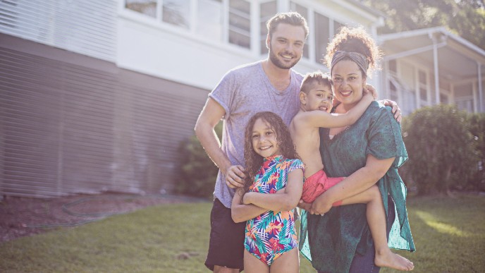 Image of a young family standing in the front yard of their new home.