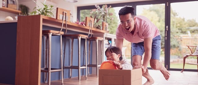 An adult pushing a child in a box through their living room.