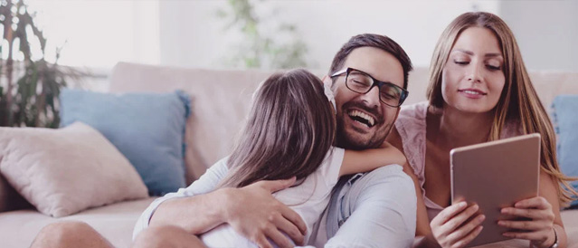 A family in their lounge room smiling while looking at a mobile device.