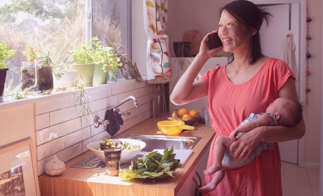 A person in a kitchen talking on a mobile phone while looking out the window.