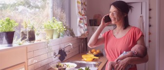 A person in a kitchen talking on a mobile phone while looking out the window.