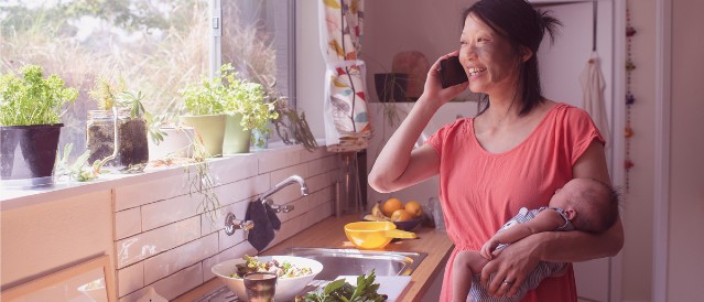 A person in a kitchen talking on a mobile phone while looking out the window.