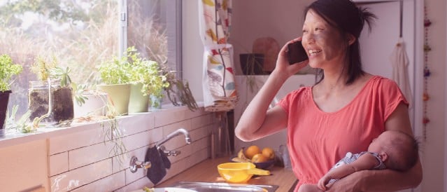 A person in a kitchen talking on a mobile phone while looking out the window.