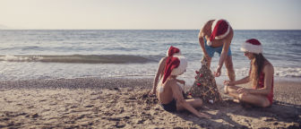 Young family on the beach in Santa hats building a Christmas sandcastle.