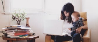 Woman sitting on couch with her toddler son looking at laptop.