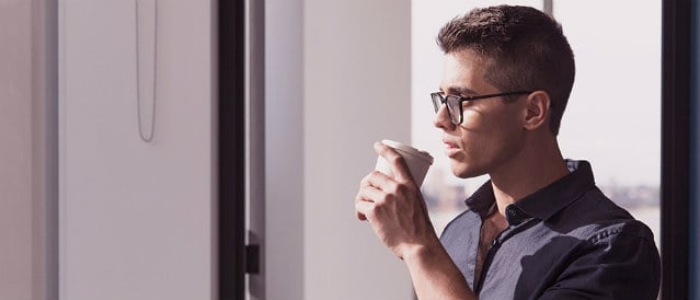 Man standing in front of window drinking coffee.