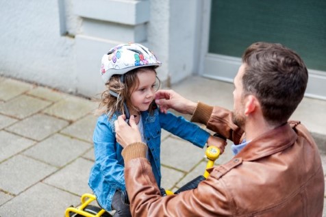 Dad helping daughter put her bike helmet on.
